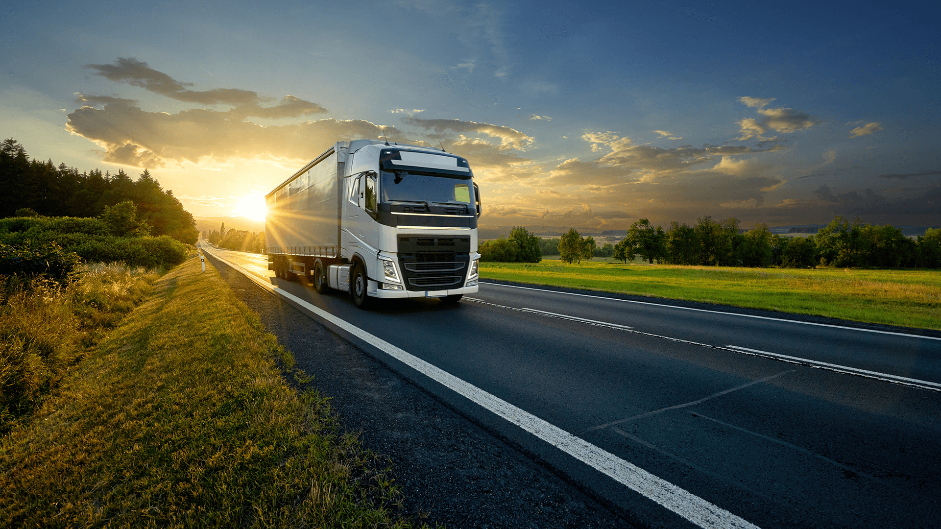 Lastebil kjører på en vei ved solnedgang med grønne omgivelser